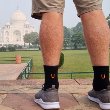 Close-up of legs wearing black socks with an orange U logo, standing in front of the Taj Mahal